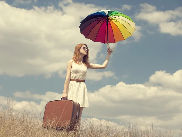 Schöne rothaarige Mädchen mit Regenschirm und Koffer im Freien. — Stockfoto