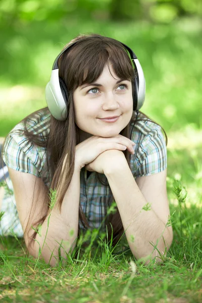 Menina de moda jovem com fones de ouvido na grama de primavera verde . — Fotografia de Stock