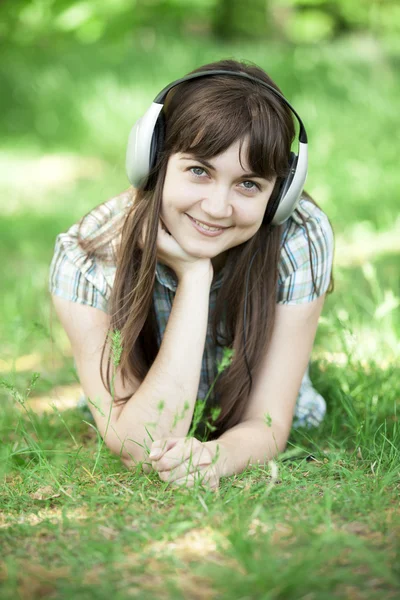 Mladá módní dívka se sluchátky na zelené jarní trávě. — Stock fotografie