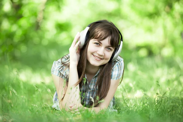 Jong mode meisje met koptelefoon op groen voorjaar gras. — Stockfoto