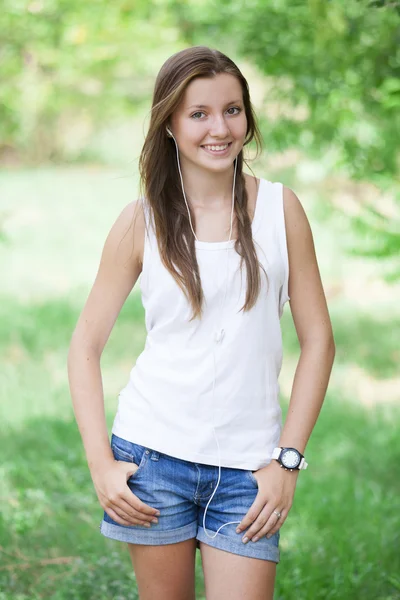 Vacker teen flicka i parken med hörlurar. — Stockfoto