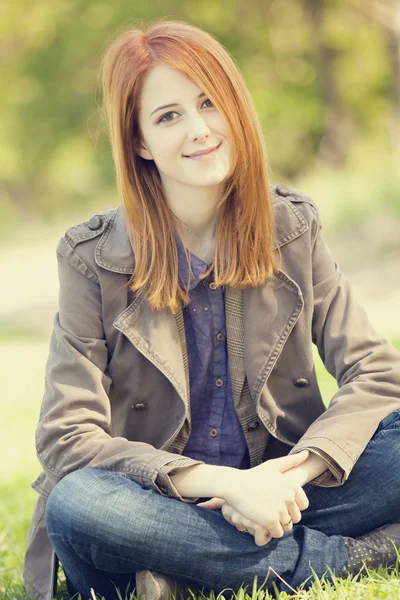 공원에서 푸른 잔디에 앉아 아름 다운 빨간 머리 소녀. — 스톡 사진