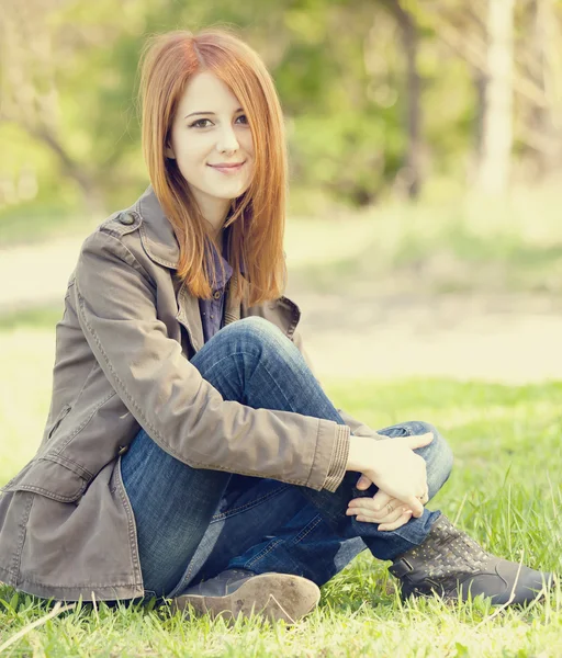 Gyönyörű vörös hajú lány ül zöld gyep a parkban. — Stock Fotó