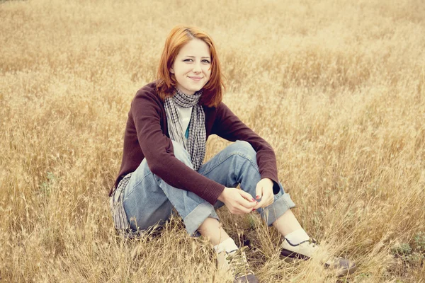 Beautiful red-haired girl at yellow autumn grass. — Stock Photo, Image