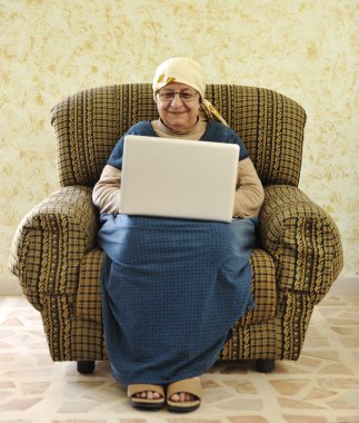 Elderly woman working on laptop in house clipart