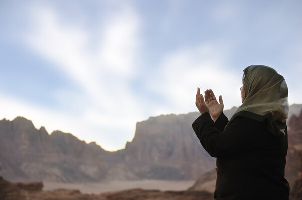 Silhouette of a muslim woman praying on the desert