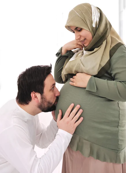 Mulher muçulmana grávida sorrindo com o marido beijando barriga, e suas mãos na barriga — Fotografia de Stock
