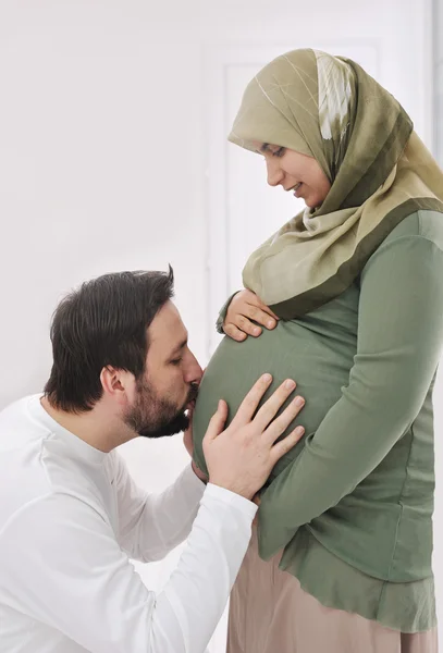 Вагітна мусульманська дружина посміхається з чоловіком цілує живіт, і його руки на животі — стокове фото