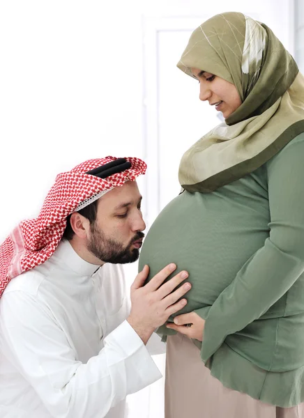 Embarazada esposa musulmana sonriendo con su marido besando vientre, y sus manos en el vientre — Foto de Stock