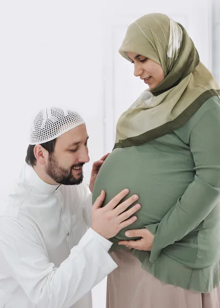 Zwangere islamitische vrouw lachend met haar echtgenoot kussen buik, en zijn handen op een buik — Stockfoto