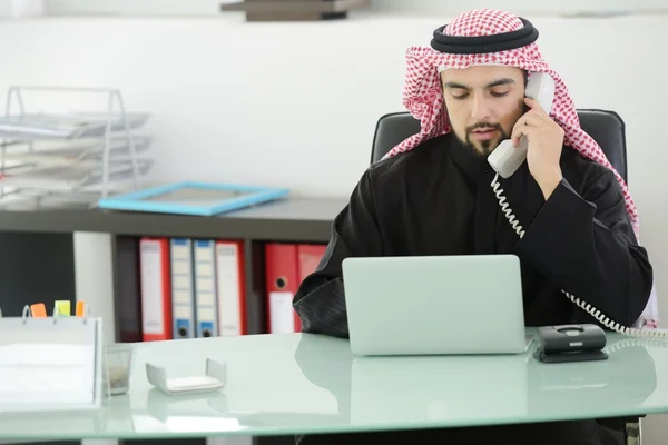 Portret van een slimme Arabische zakenman met behulp van laptop en praten over de telefoon — Stockfoto