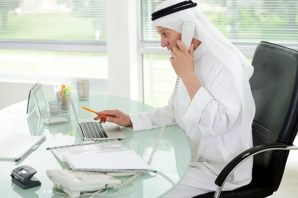Porträt eines smarten arabischen Geschäftsmannes, der Laptop benutzt und am Telefon spricht — Stockfoto