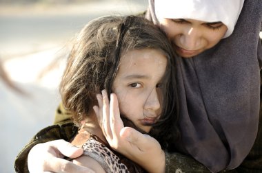 Poverty and poorness on the children face. Sad little girl. Refugee. In Muslim mother's arms. clipart