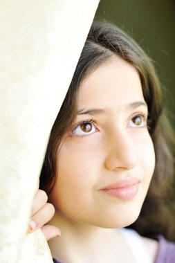 Little beautiful girl sitting at window and holding curtain, portrait clipart