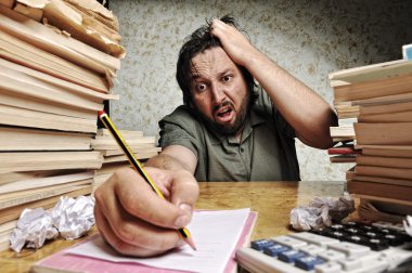Accountant in problems. Alone working in office with a lot of books around on messy table. Yelling and screaming for bad results.