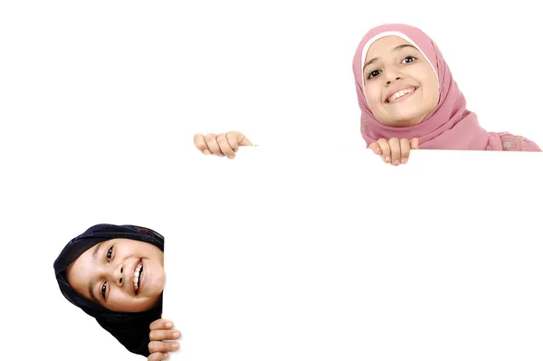 Две маленькие школьницы держат белый знак для твоего сообщения. Хорошо подходит для границ статей или веб-сайтов. Красивые арабские мусульманские модели. Изолированный на белом фоне . — стоковое фото