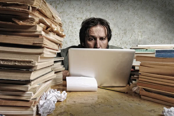 Бухгалтер в проблемах. Один працює на ноутбуці з великою кількістю книг навколо на брудному столі . — стокове фото