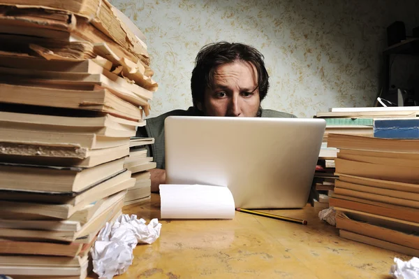 Uomo d'affari che lavora in ufficio sul portatile. tavolo disordinato con un sacco di libri su . — Foto Stock