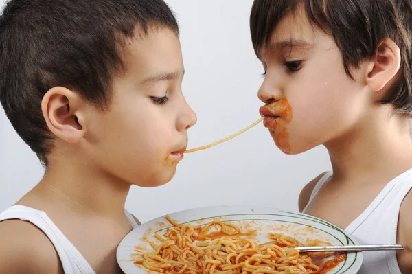 Dos niños comiendo espaguetis uno contra el otro. —  Fotos de Stock