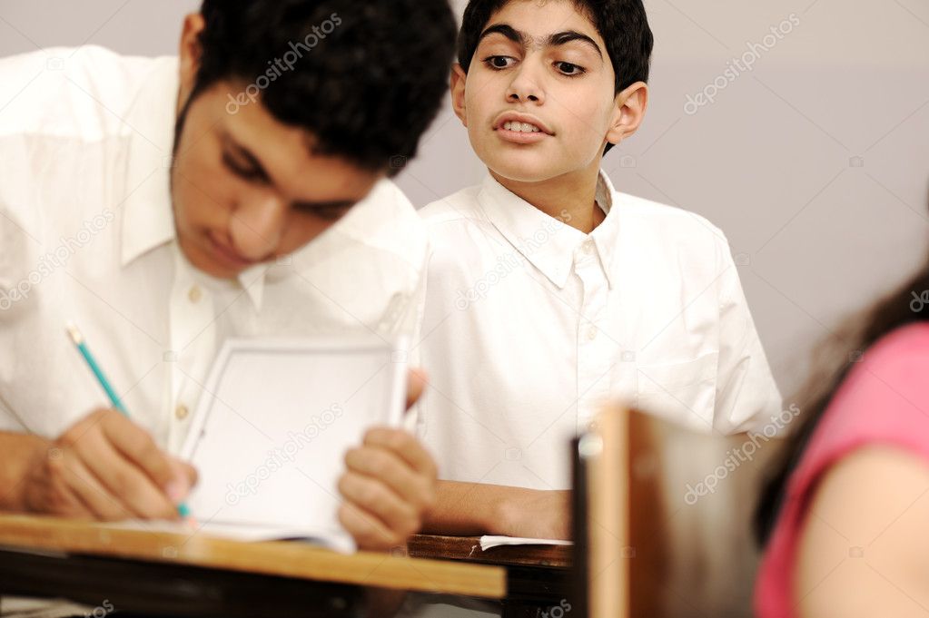 Cheating inside the classroom while the exam is present, boy looking above the shoulder of his colleague.