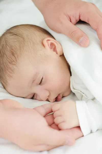 Újszülött baba, az édesanyja kezét, alszik az ágyban — Stock Fotó