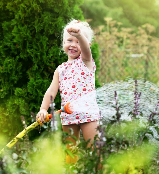 Egy kislány locsolja a füvet a kertben. — Stock Fotó