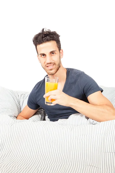 Усміхнений чоловік п'є апельсиновий сік у ліжку — стокове фото