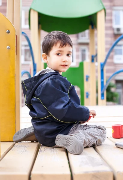 Rapaz senta-se no parque infantil — Fotografia de Stock