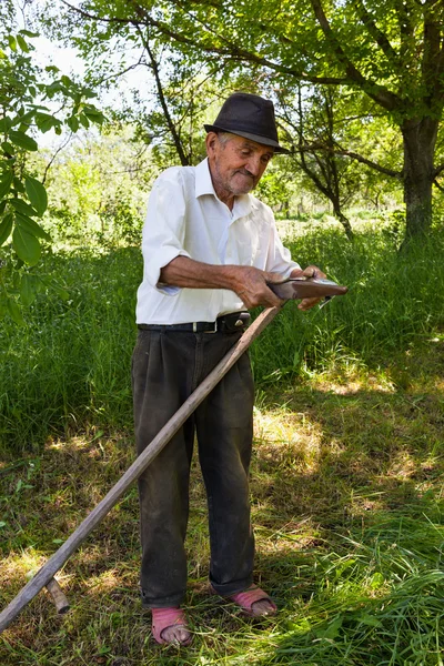 Starý muž broušení kosy — Stock fotografie