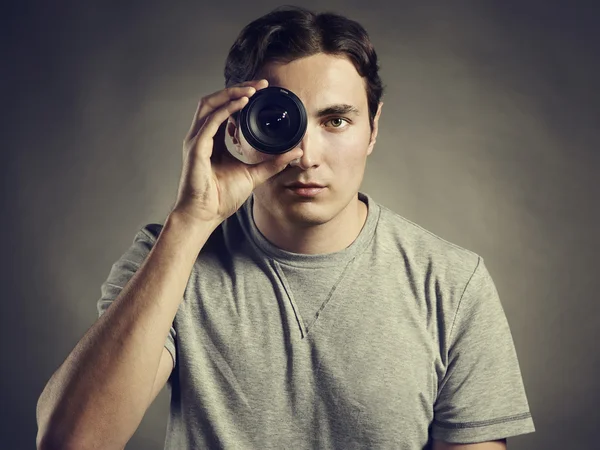 Young man photographer holding a lens in his eye — Stock Photo, Image