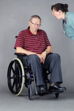Tekerlekli sandalyedeki üzgün yaşlı adama hemşire tarafından bağırılıyor.