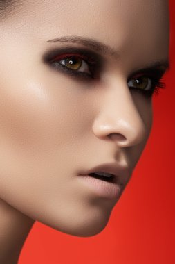 Close-up portrait of beautiful young woman model on bright red background. Dark fashion smoky eyes make-up, pale lips and smooth skin clipart