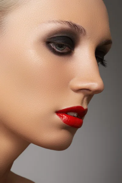 Retrato de beleza close-up de rosto modelo atraente com visagem de moda. Maquiagem de olho esfumaçado escuro e maquiagem de lábios vermelhos brilhantes — Fotografia de Stock