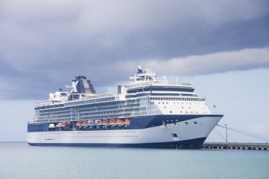 Blue and White Cruise Ship Tied to Pier Under Cluds clipart