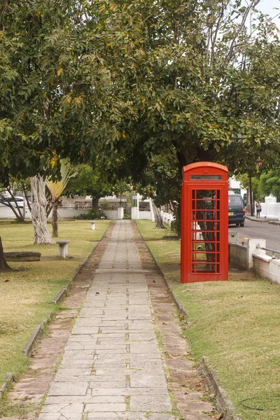Röd telefonkiosk av trottoaren genom park — Stockfoto