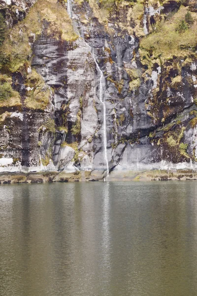 Wasserfall an Felsen vorbei ins grüne Wasser — Stockfoto