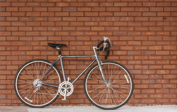 Bicicleta velha encostada à parede de tijolo vermelho — Fotografia de Stock