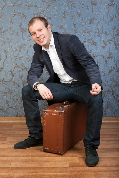 Mladý muž sedí na staré hnědé kufr v interiéru — Stock fotografie