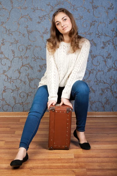 Beautiful young girl sitting on an old brown suitcase in the int — Stock Photo, Image