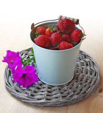 Berries of strawberry in a grey bucket and flowers