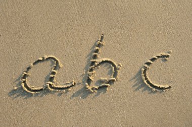 Alphabet letters handwritten in sand on beach clipart