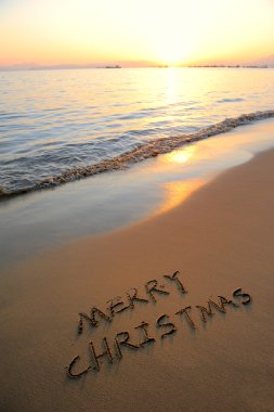 Merry Christmas handwritten in sand on a beautiful beach clipart