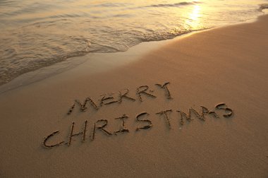 Merry Christmas handwritten in sand on beach clipart