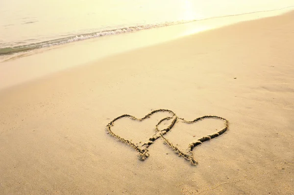 Två hjärtan dras på sanden på en strand — Stockfoto
