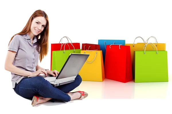 Jovem mulher bonita usando um laptop para compras on-line com sacos de compras 3d no fundo — Fotografia de Stock