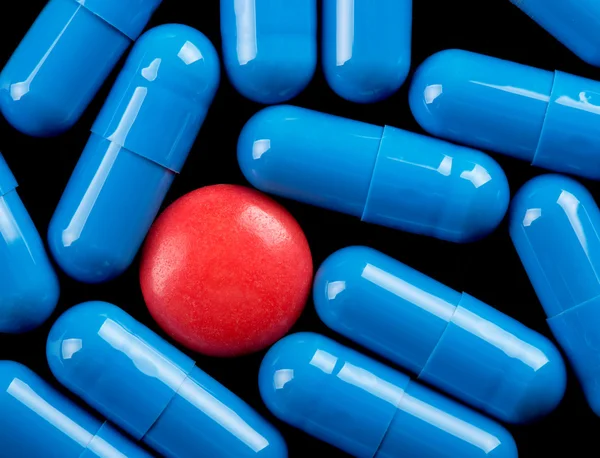 Красная таблетка между голубыми капсулами — стоковое фото