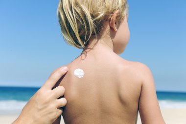 Mother applying sunscreen on childs back clipart