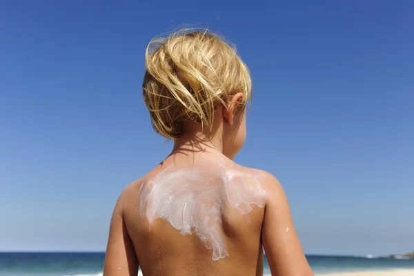 Мила дитина з сонцезахисним кремом на пляжі — стокове фото