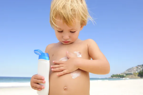Lindo niño aplicando protector solar en la playa — Foto de Stock