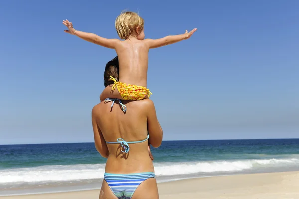 Мать несет свою дочь на плечах на пляже — стоковое фото